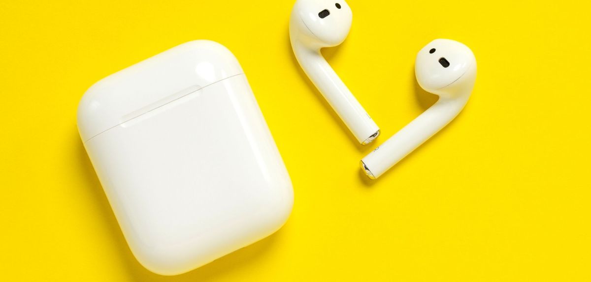 AirPods mit Ladeschatulle auf gelbem Untergrund.