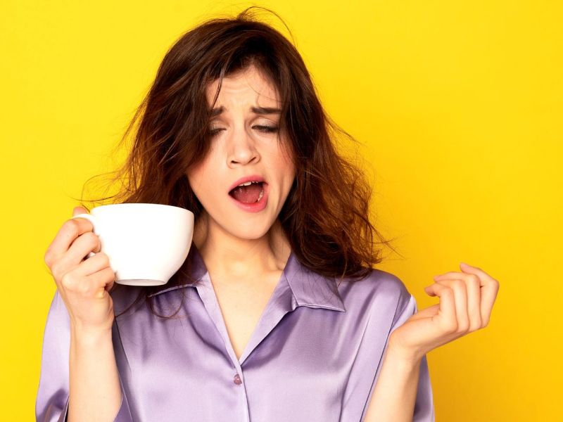 Frau gähnt mit einer Tasse Kaffee in der Hand.