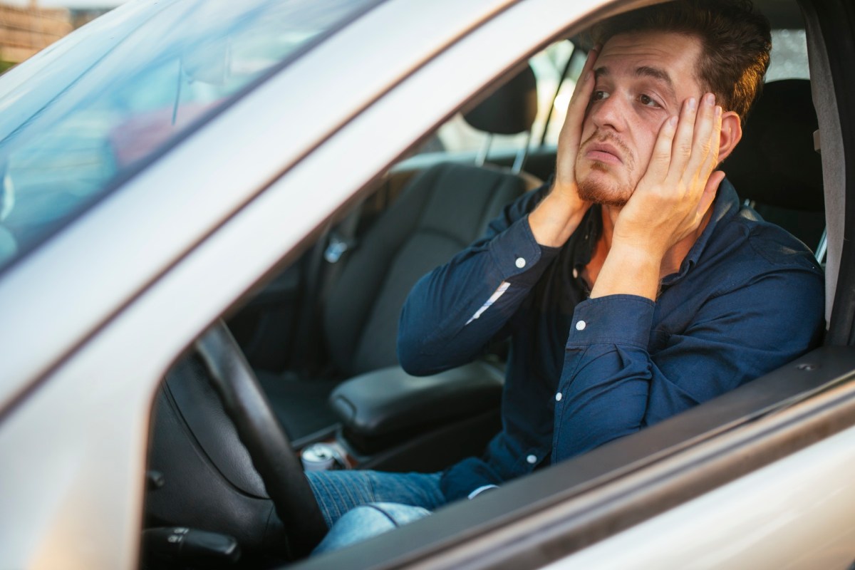 Mann im Stau im Auto hält sich aus Frust das Gesicht