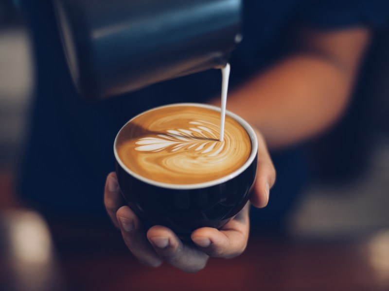 Milch wird in eine Tasse Kaffee gegossen.