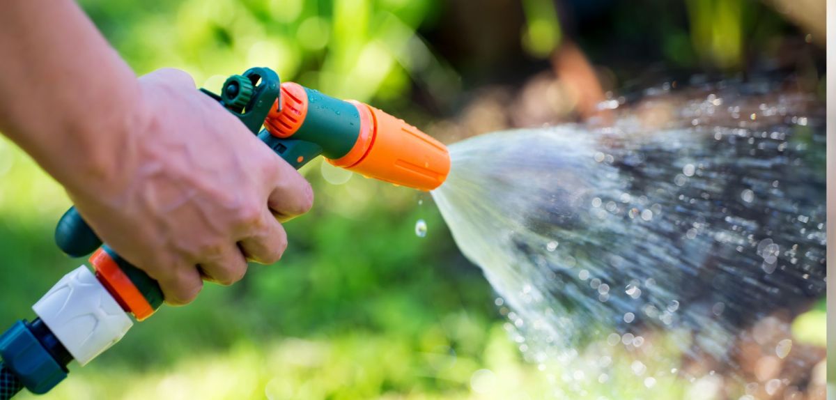 Person bewässert mit Wasserschlauch den Garten.