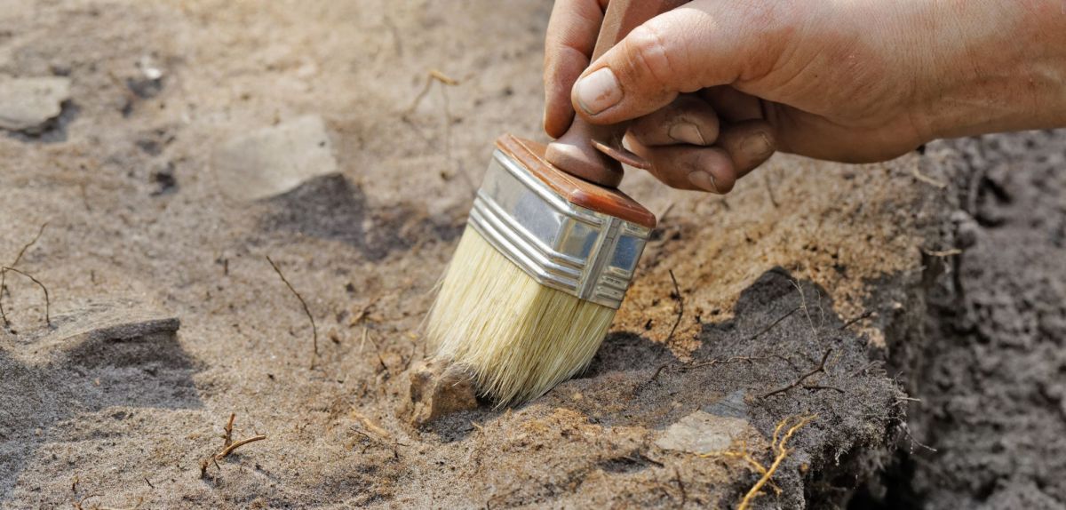 Person nutzt einen Pinsel bei einer archäologischen Ausgrabung.