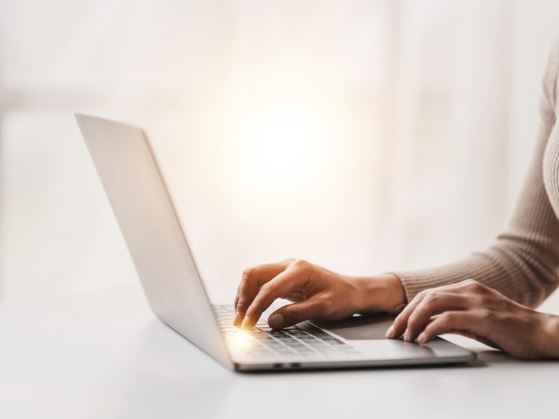 Eine Frau sitzt am Tisch und schreibt auf ihrem Laptop.