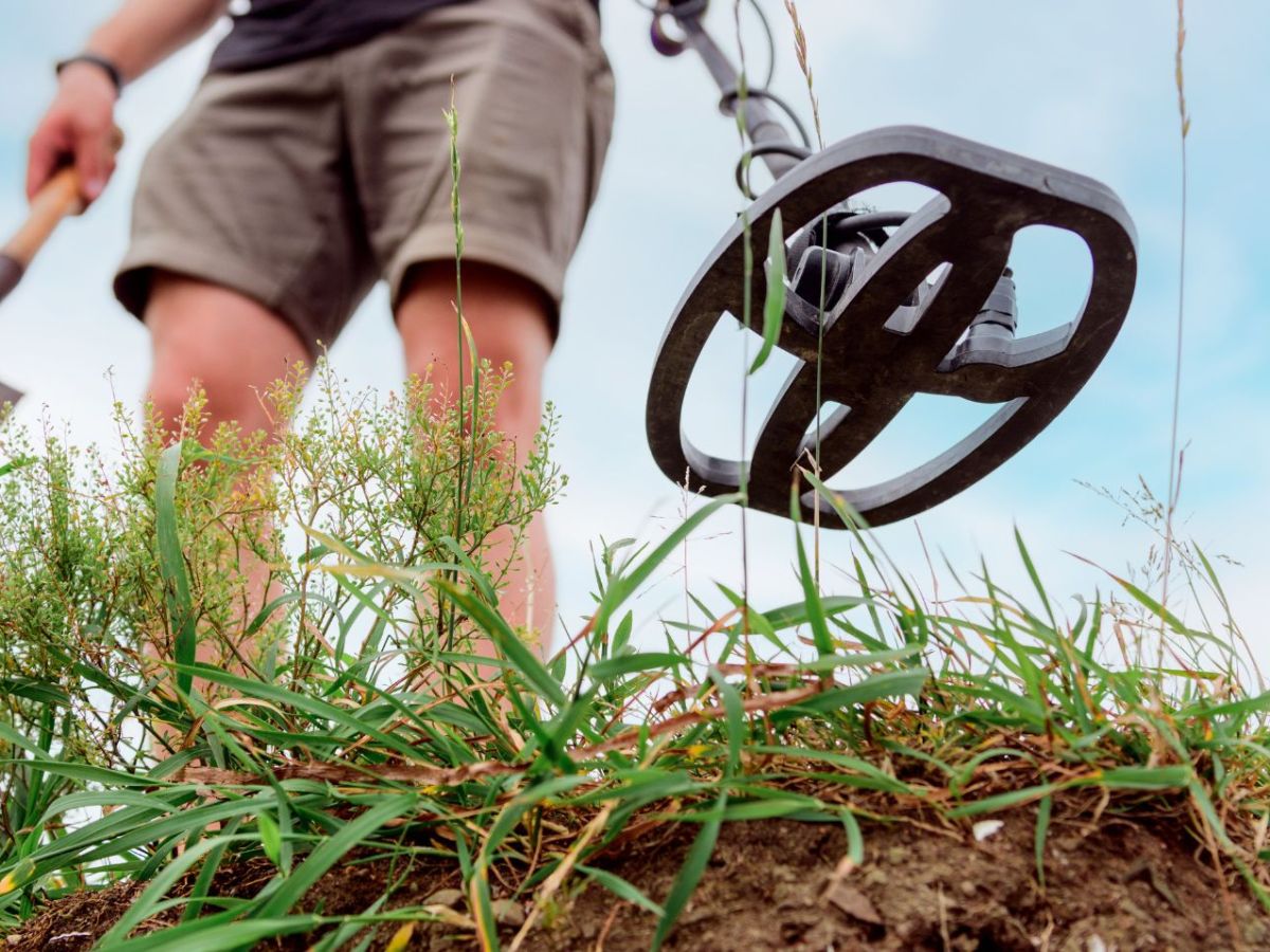 Mann mit Schaufel und Metalldetektor auf einem Feld.