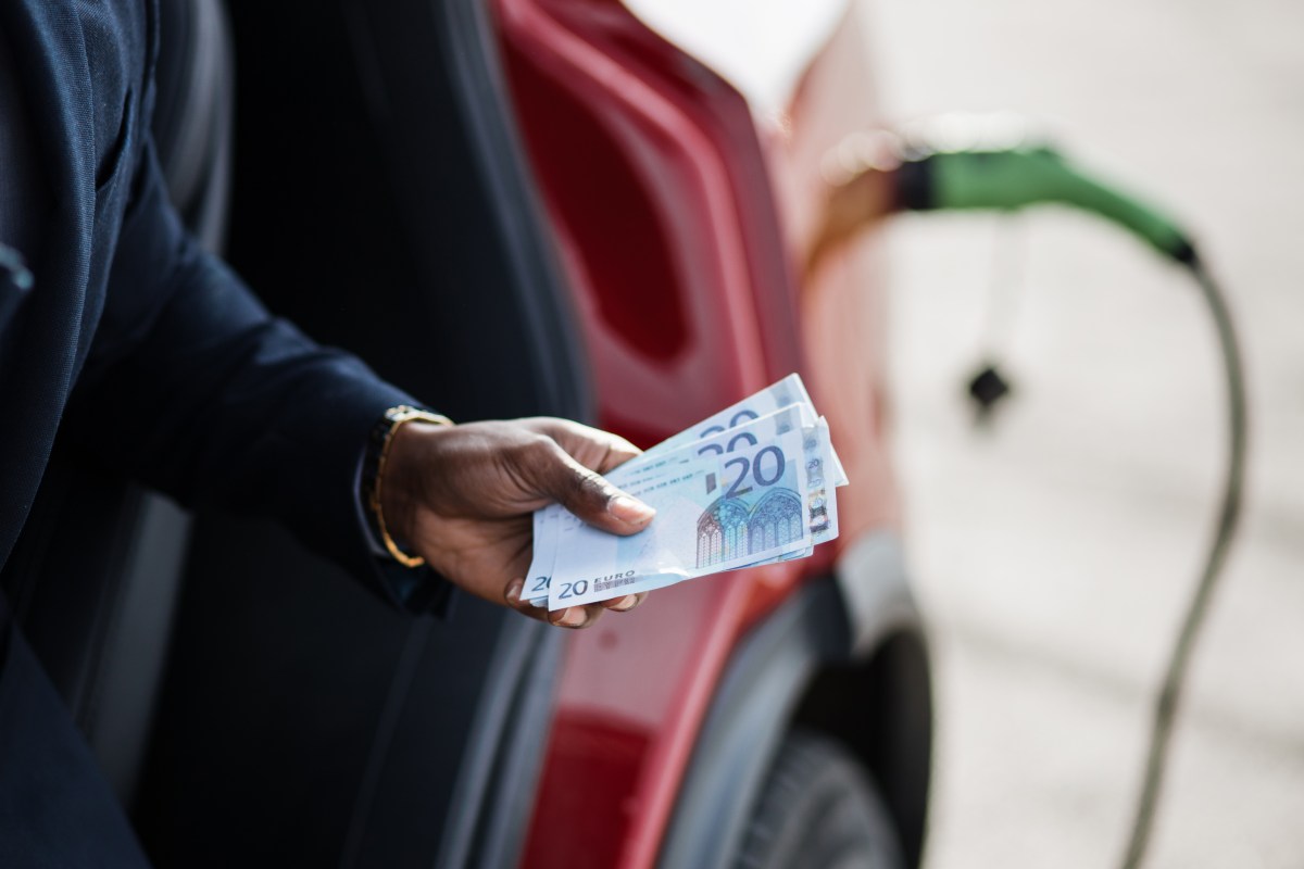 Person mit Geldscheinen in der Hand vor einem ladenden Elektroauto