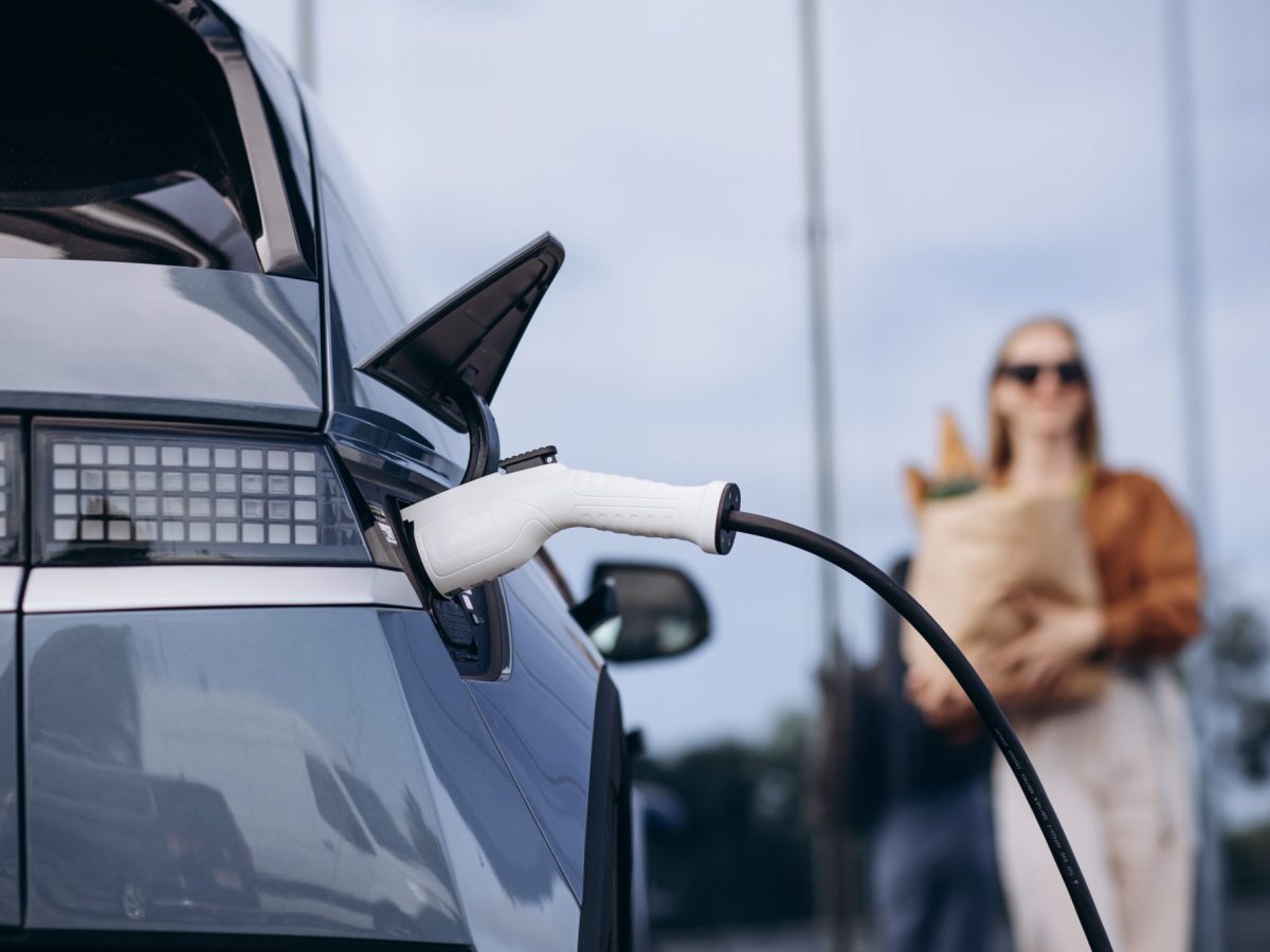 Eine Frau trägt ihre Einkäufe während sich ihr Elektroauto auflädt.