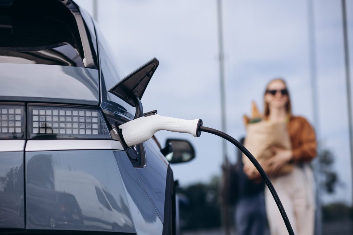 Eine Frau trägt ihre Einkäufe während sich ihr Elektroauto auflädt.