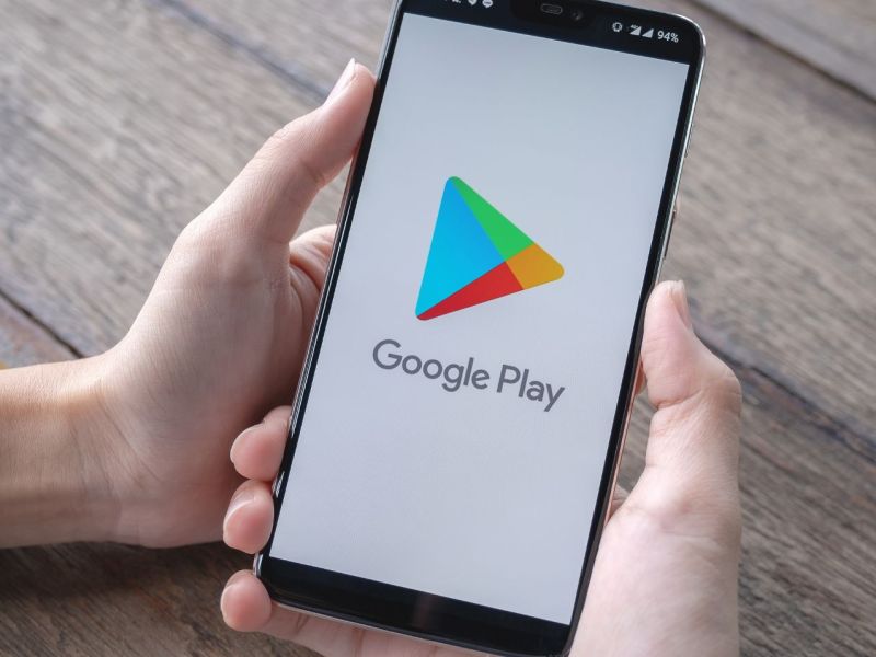 Person hält Handy mit dem Google Play Store auf dem Bildschirm in der Hand.