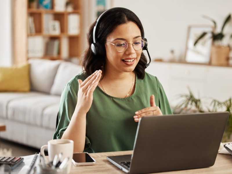 Frau sitzt vor einem Laptop und telefoniert mit Headset.