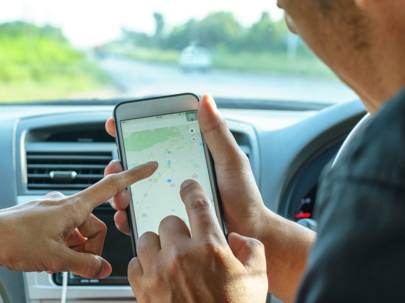 Mann und Frau deuten in Auto auf Google Maps auf dem Handy.