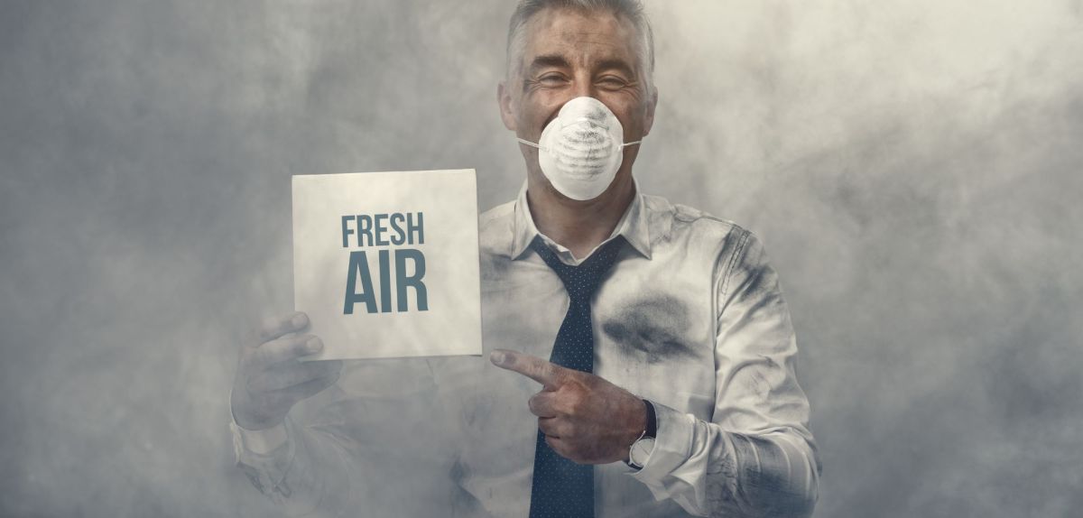 Mann mit Atemmaske im Gesicht hält ein Schild hoch mit der Aufschrift: "Fresh Air".