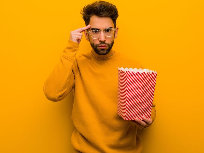 Mann hält eine Tüte Popcorn in der Händ und zeigt auf seinen Kopf.