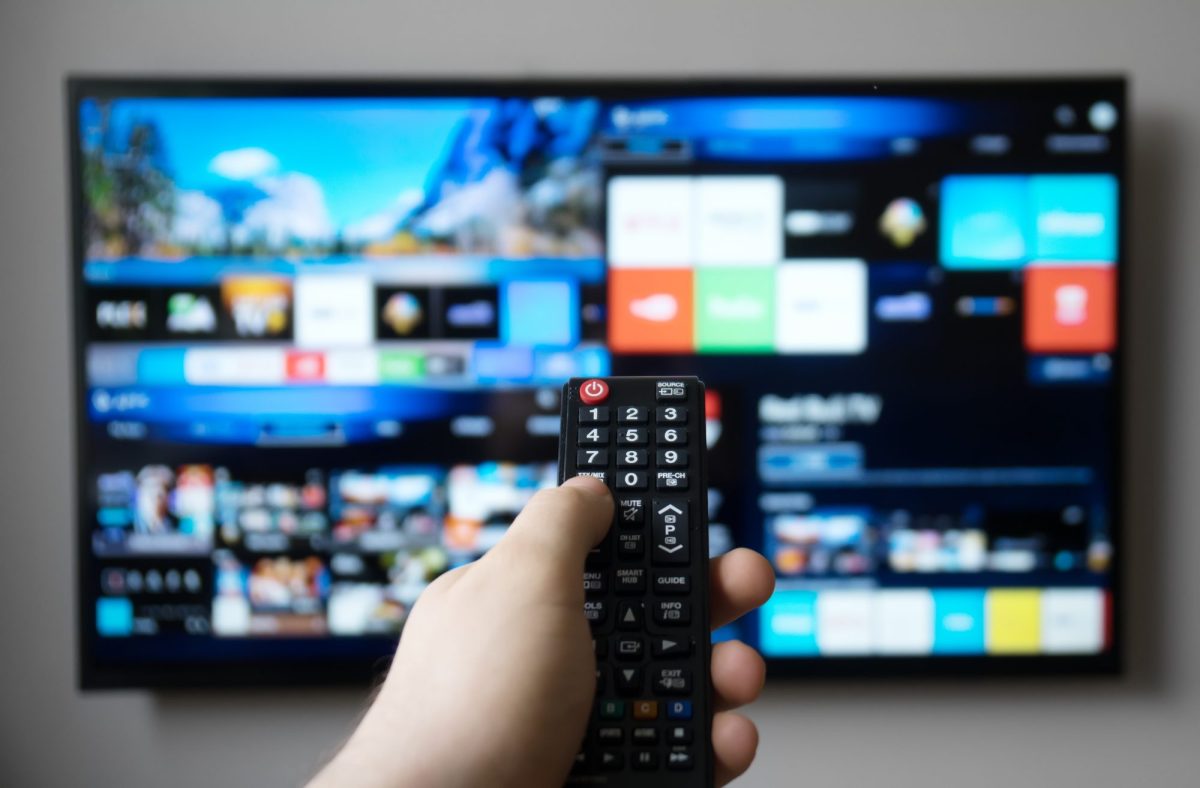 Hand bedient Fernbedienung, die auf einen Smart TV gerichtet ist.