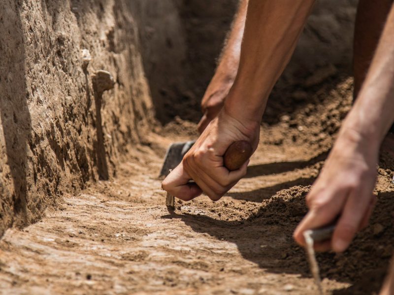 Hände graben mit Werkzeugen an archäologischem Fund.