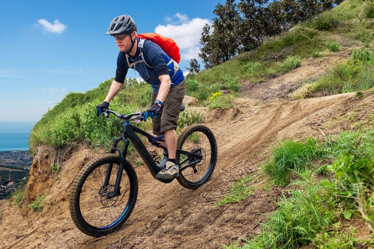 Mann fährt auf Trekking-E-Bike einen Berg herunter.