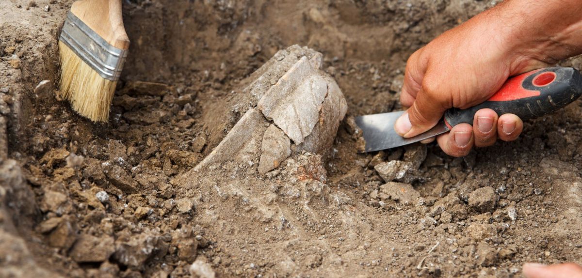 Hände mit Werkzeugen graben an einem archäologischen Fund.