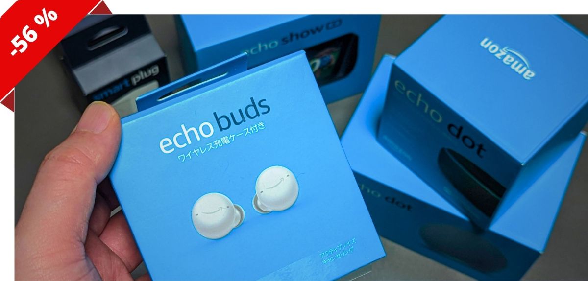 Eine Hand hält eine Packung Amazon Echo Buds. Dahinter liegen andere Produkte von Amazon.