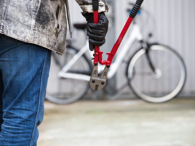 Person hält eine Zange. Im Hintergrund steht ein Fahrrad an einer Wand.