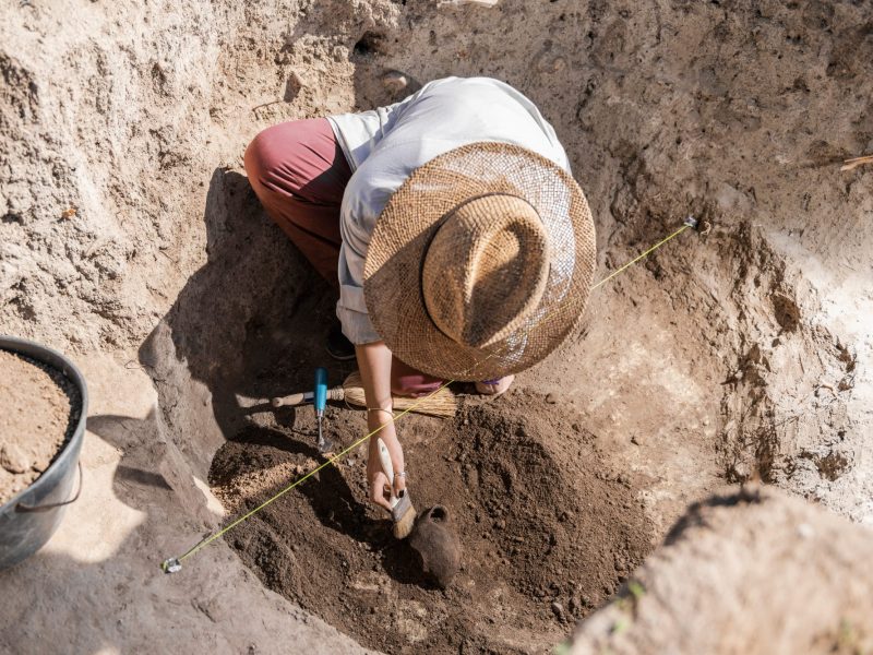 Frau arbeitet mit Werkzeug an einem archäologischen Fund.
