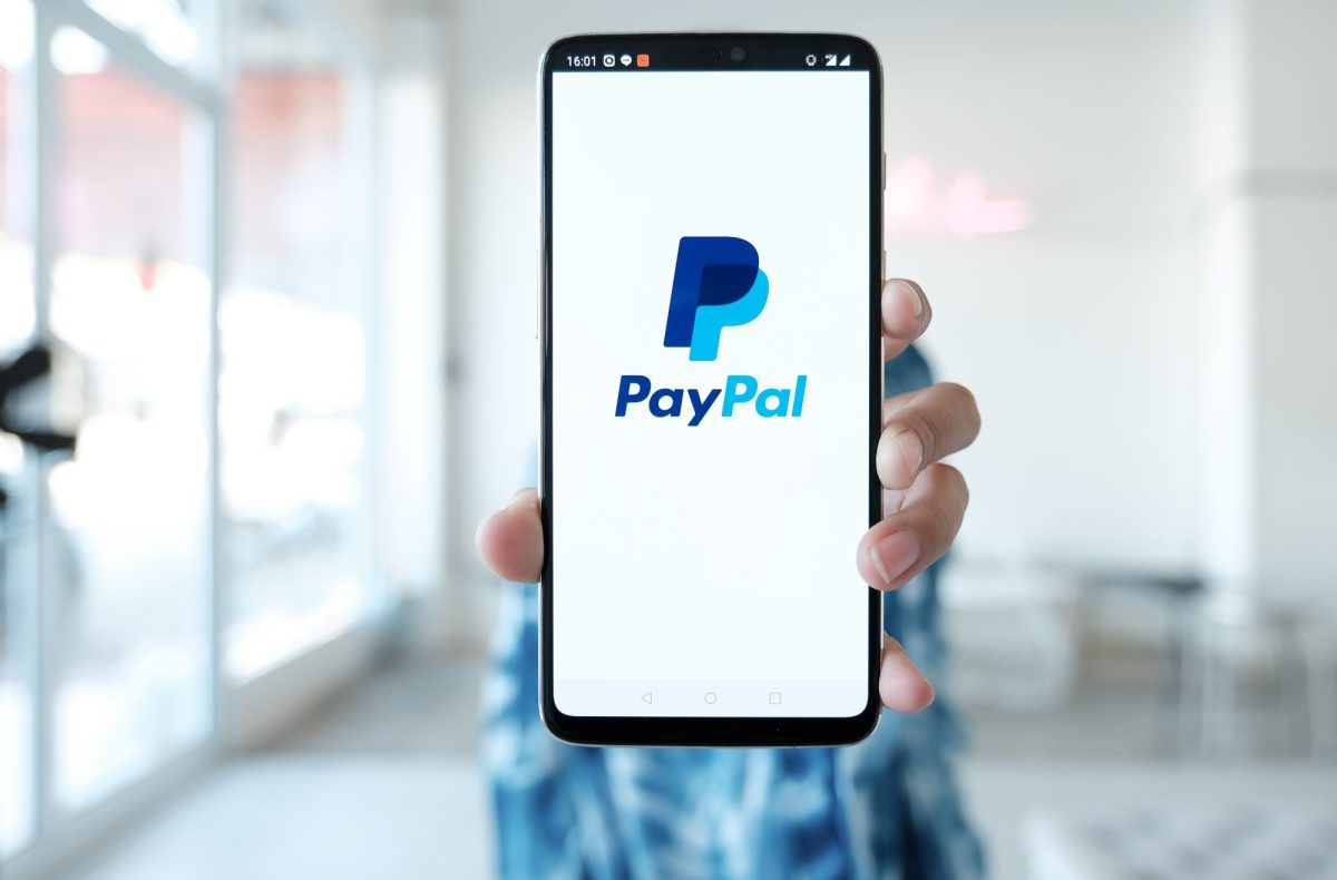 Eine Person hält ein Handy. Auf dem Display wird das PayPal-Logo angezeigt.
