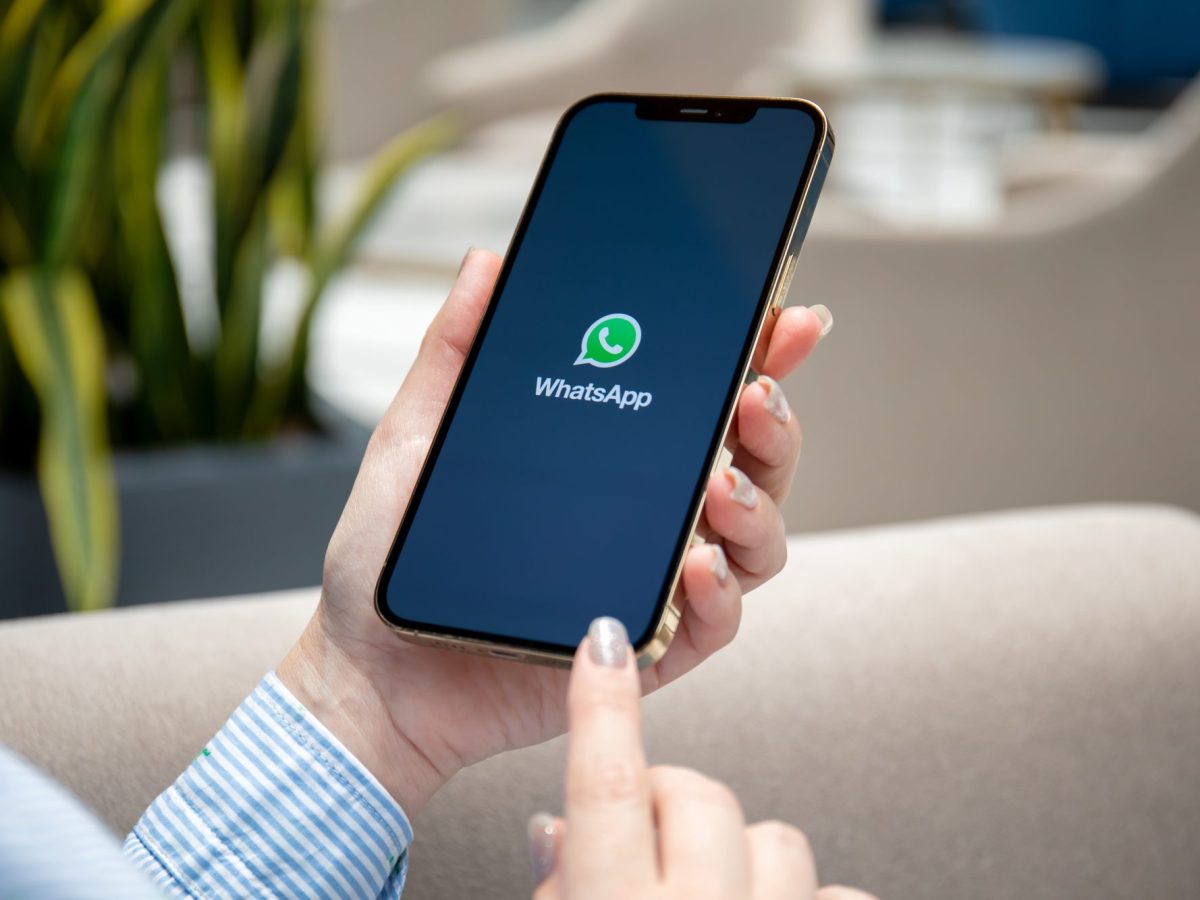 Eine Person hält ein Handy, auf dessen Display das WhatsApp-Logo angezeigt wird.