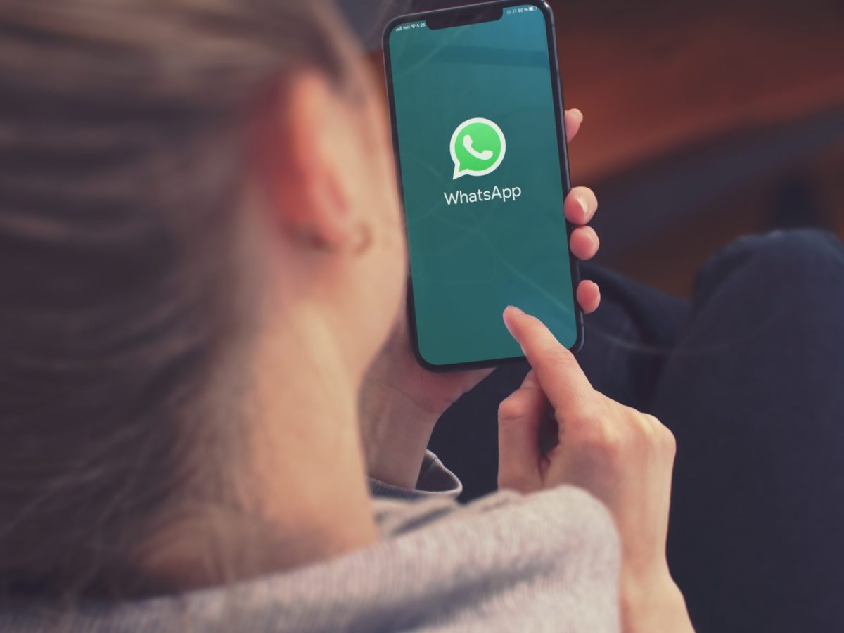 Eine Frau hält ein Handy in der Hand. Auf dem Display ist das WhatsApp-Logo zu sehen.