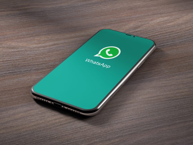Ein Handy liegt auf einer Holzoberfläche. Auf dem Display wird das WhatsApp-Logo angezeigt.