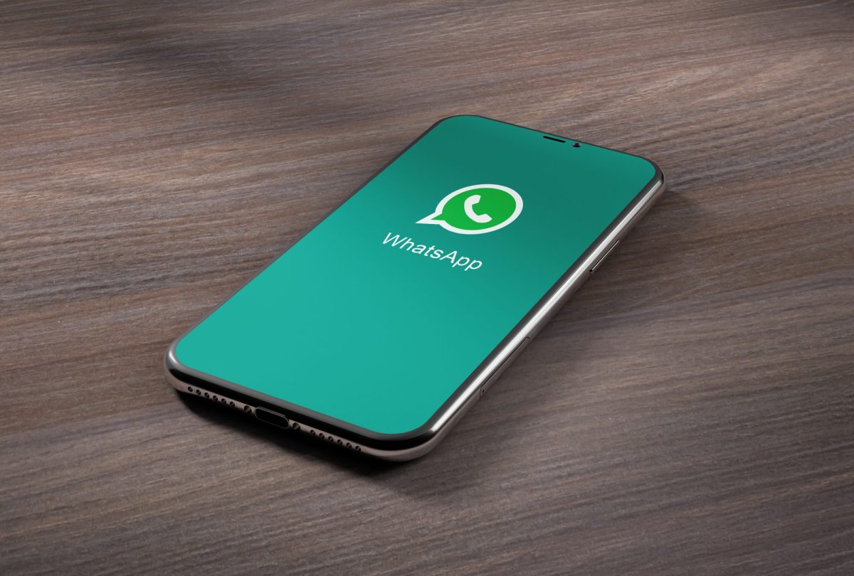 Ein Handy liegt auf einer Holzoberfläche. Auf dem Display wird das WhatsApp-Logo angezeigt.