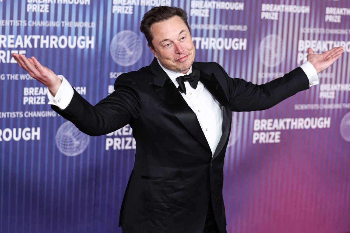 Portrait von Elon Musk auf rotem Teppich mit hochgezogenen Schultern und Armen