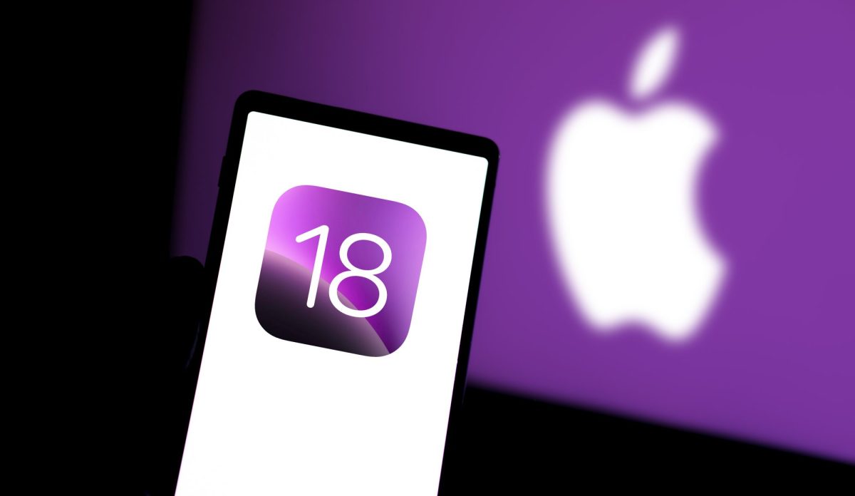 Handy zeigt iOS-18-Logo, im Hintergrund ist ein Apple-Logo zu sehen.