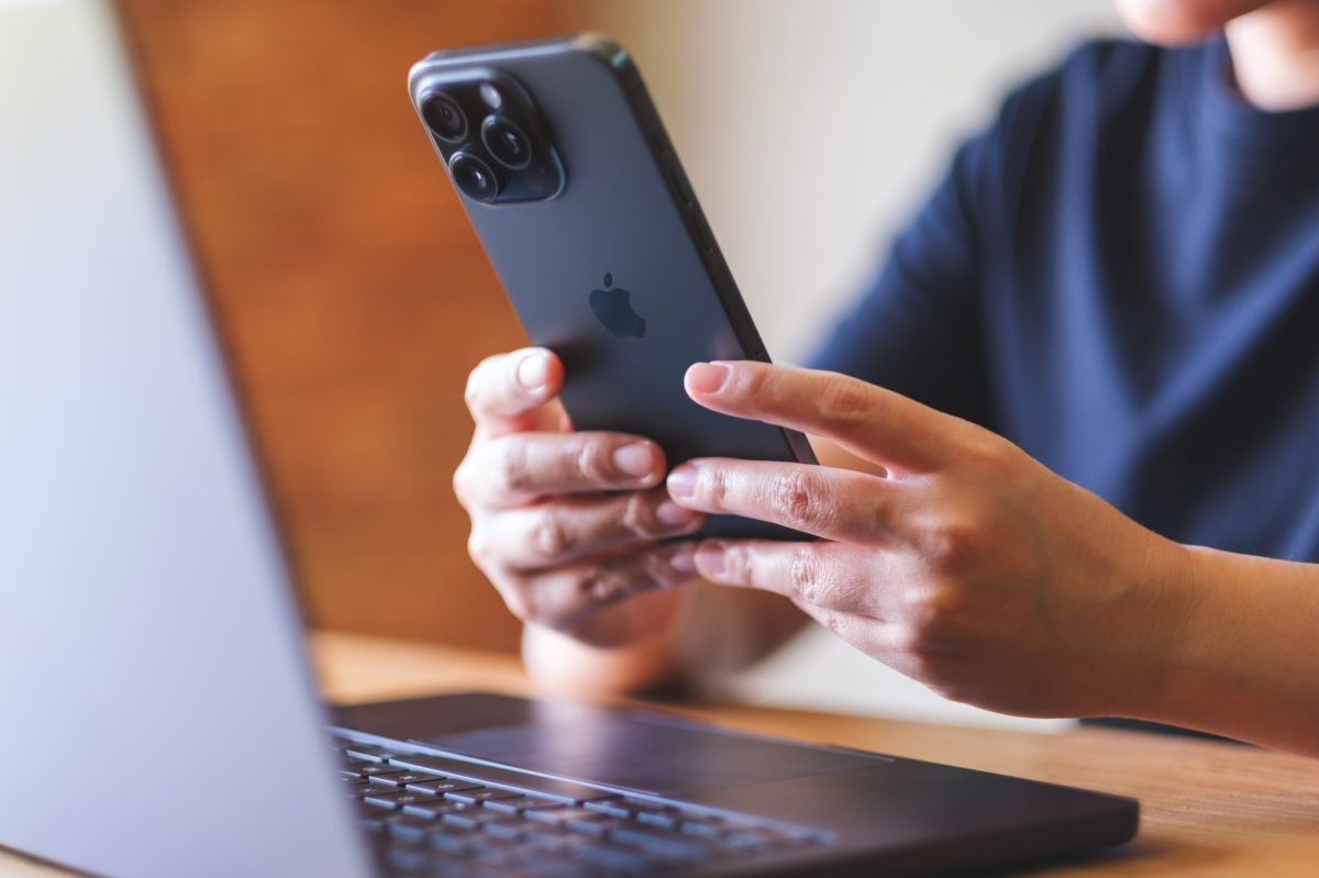 Person sitzt vorm Laptop und hält iPhone in der Hand