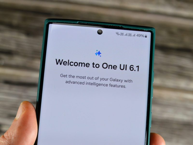 Person hält ein Samsung Galaxy in der Hand. Auf dem Display steht "Welcome to One UI 6.1"