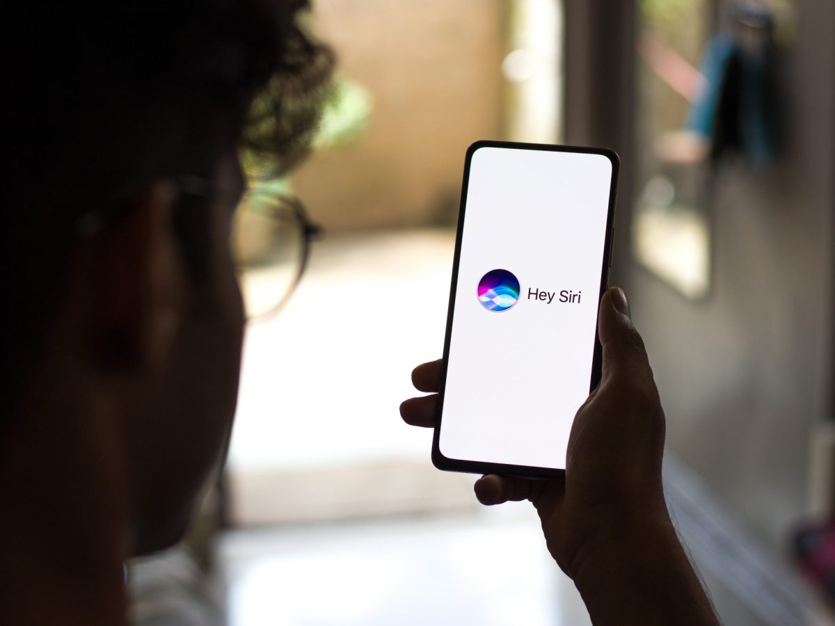 Eine Person hält ein Handy in der Hand, auf dessen Display Hey Siri angezeigt wird.