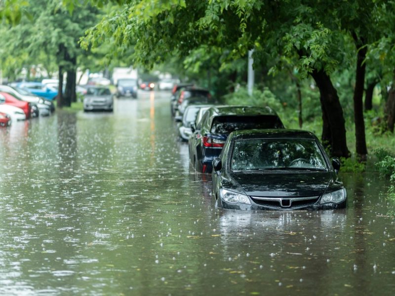 Überschwemmung auf einer Straße mit parkenden Autos. (