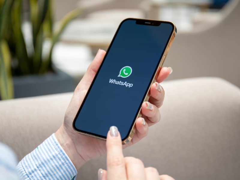 Eine Frau hält ein Smartphone in der Hand, auf dessen Display das WhatsApp-Logo angezeigt wird.