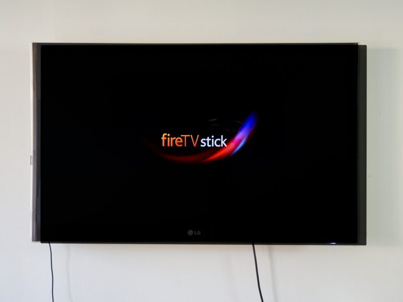 Ein Fernseher ist an der Wand befestigt, darauf ist das Logo des Amazon Fire TV Stick zu sehen.