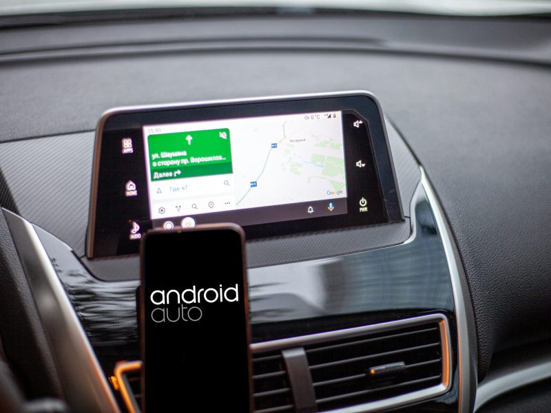 Android Auto auf einem Handy-Display. Im Hintergrund ist das Armaturenbrett eines Autos zu sehen.