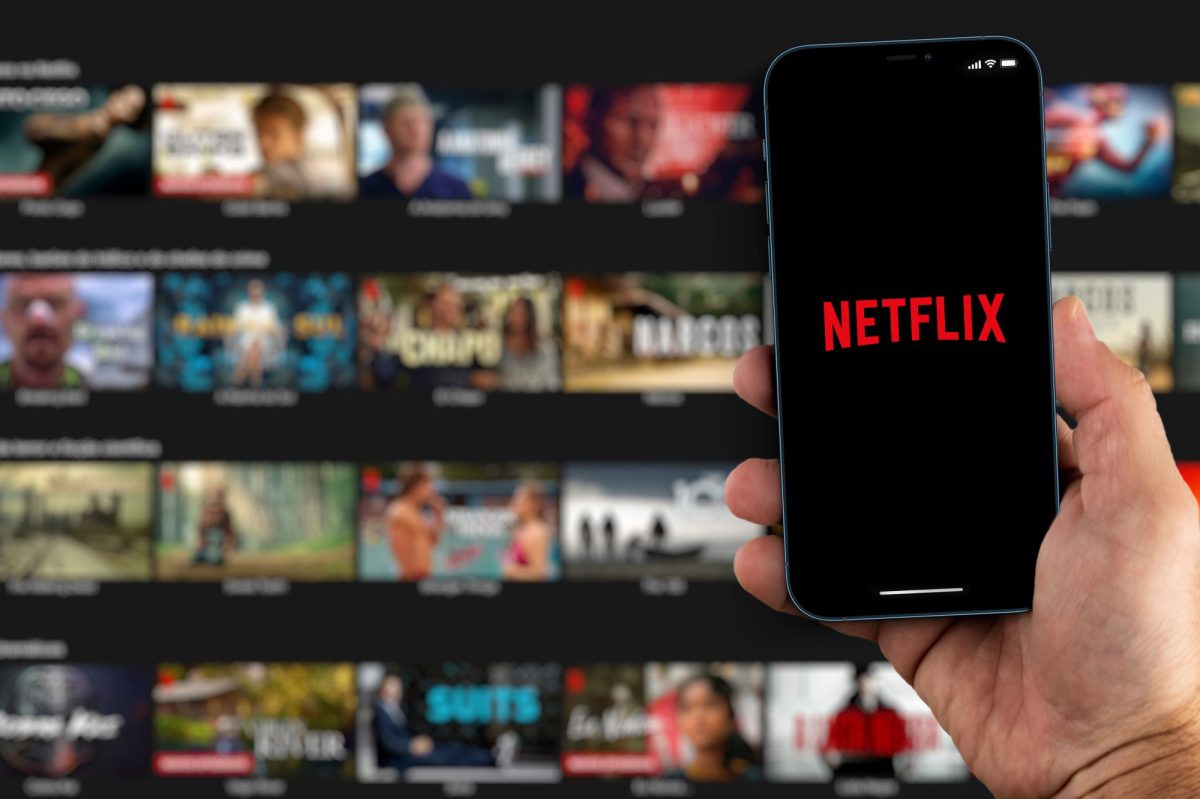 Handy zeigt Netflix-Logo vor einem Fernseher als Hintergrund.