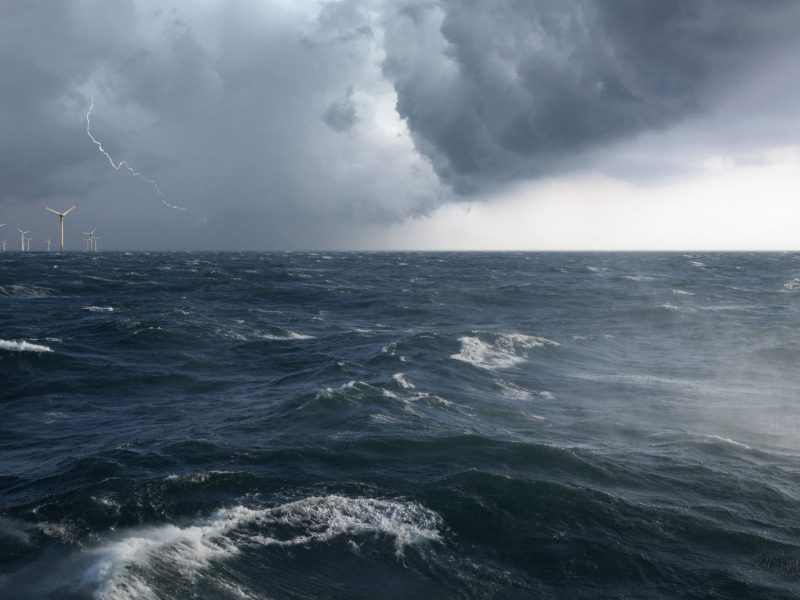 Ein Offshore Windpark mit aufgewühlter See in einem Sturm mit Blitz.