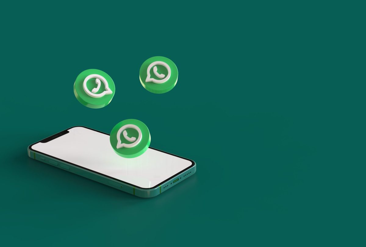 Ein Handy liegt auf einem grÃ¼nen Untergrund. DarÃ¼ber schweben drei WhatsApp-Logos.