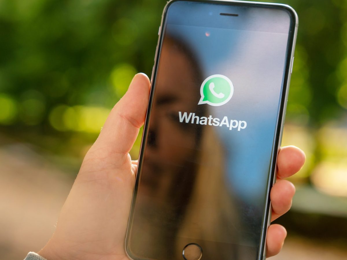 Eine Person hält ein Handy. Auf dessen Display wird das WhatsApp-Logo angezeigt.