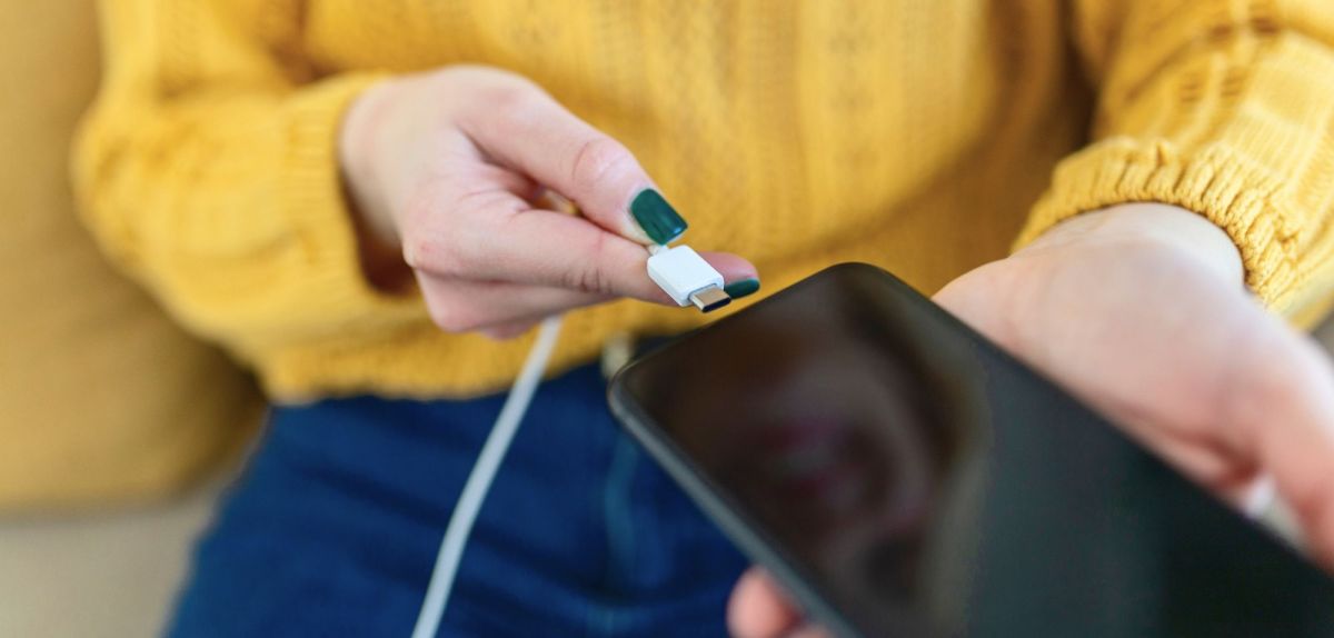 Frau steckt Handy ans Ladekabel