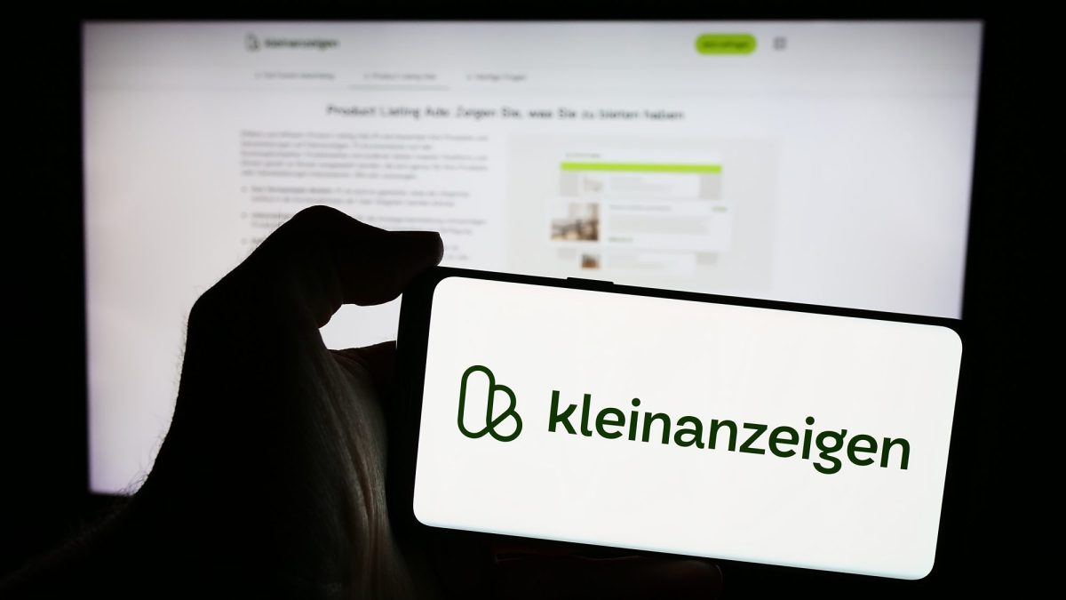 Person hält ein Smartphone in der Hand, auf dem Bildschirm ist das Logo von Kleinanzeigen zu sehen,