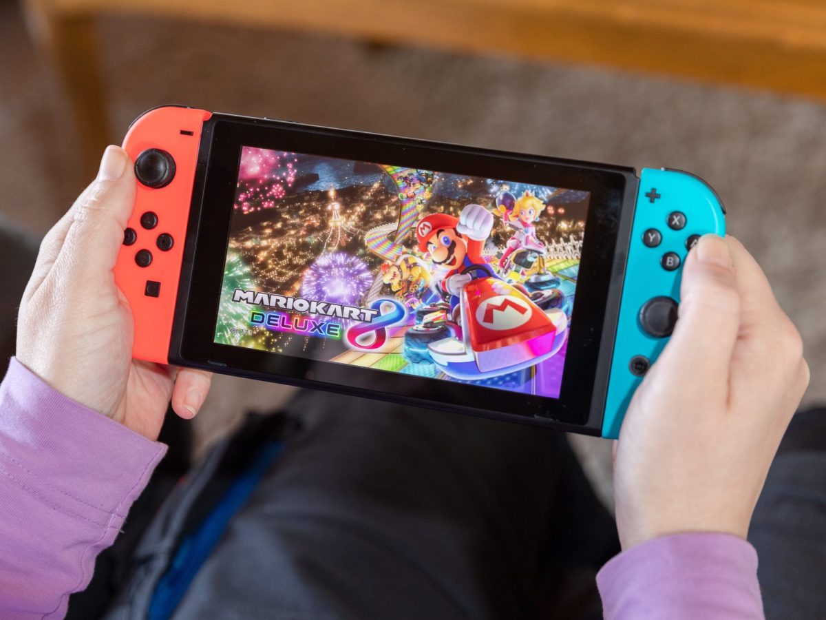 Person hält eine Nintendo Switch in der Hand, auf der Mario Kart läuft.