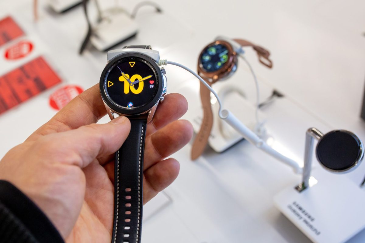 Eine Person hÃ¤lt eine Samsung Galaxy Watch in der Hand. Im Hintergrund sind in einer Auslage weitere Samsung Galaxy Watch-Modelle zu sehen.