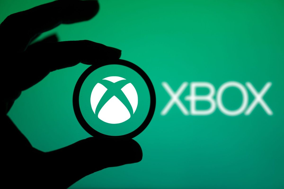 Das Xbox-Logo ist auf einem grÃ¼nen Hintergrund zu sehen. Im Vordergrund ist der Schatten einer Hand zu sehen.