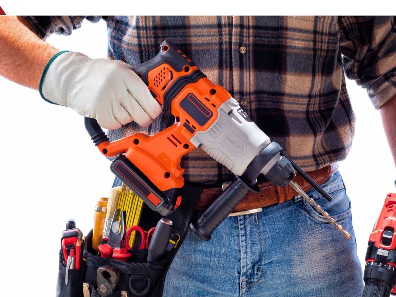 Eine Person mit Werkzeuggürtel hält einen Akku-Bohrhammer in der Hand.