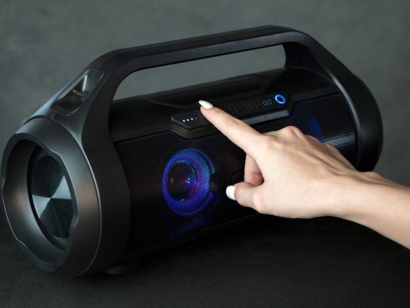 Person drückt auf eine Taste eines Bluetooth-Laustprechers.