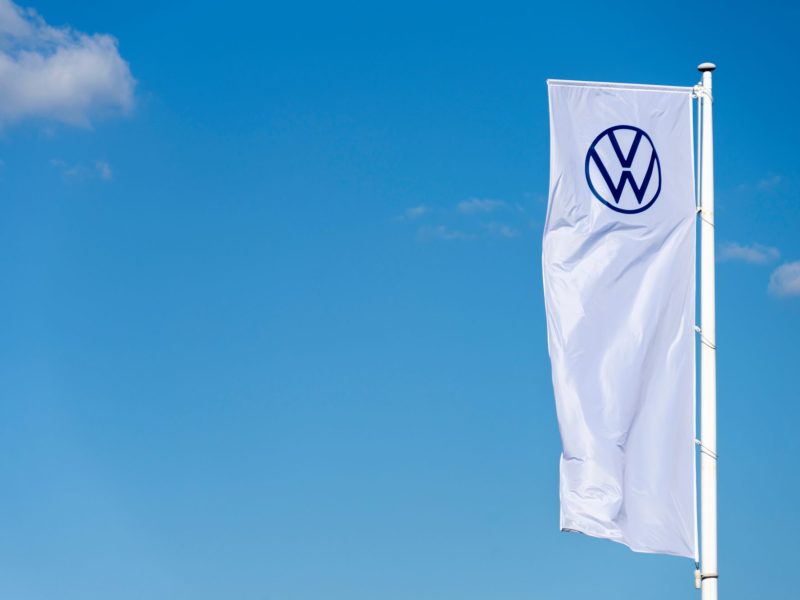 Weiße Fahne mit VW-Logo vor blauem Himmel.