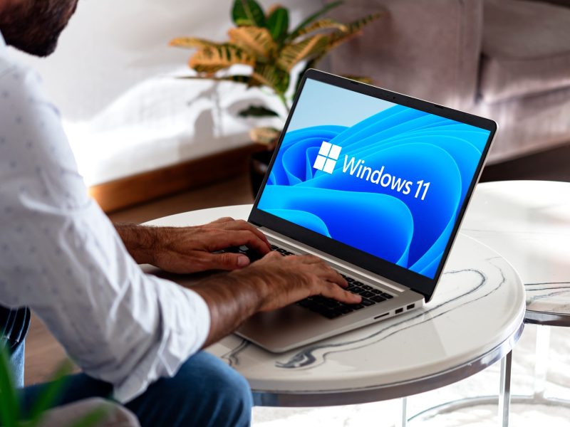 Person bedient einen Laptop, auf dessen Bildschirm, das Windows 11-Logo angezeigt wird.